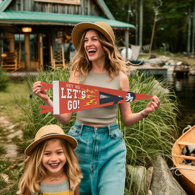A woman and a young girl are standing near a lake, holding a red and white sign that says "Hey ho let's go!"