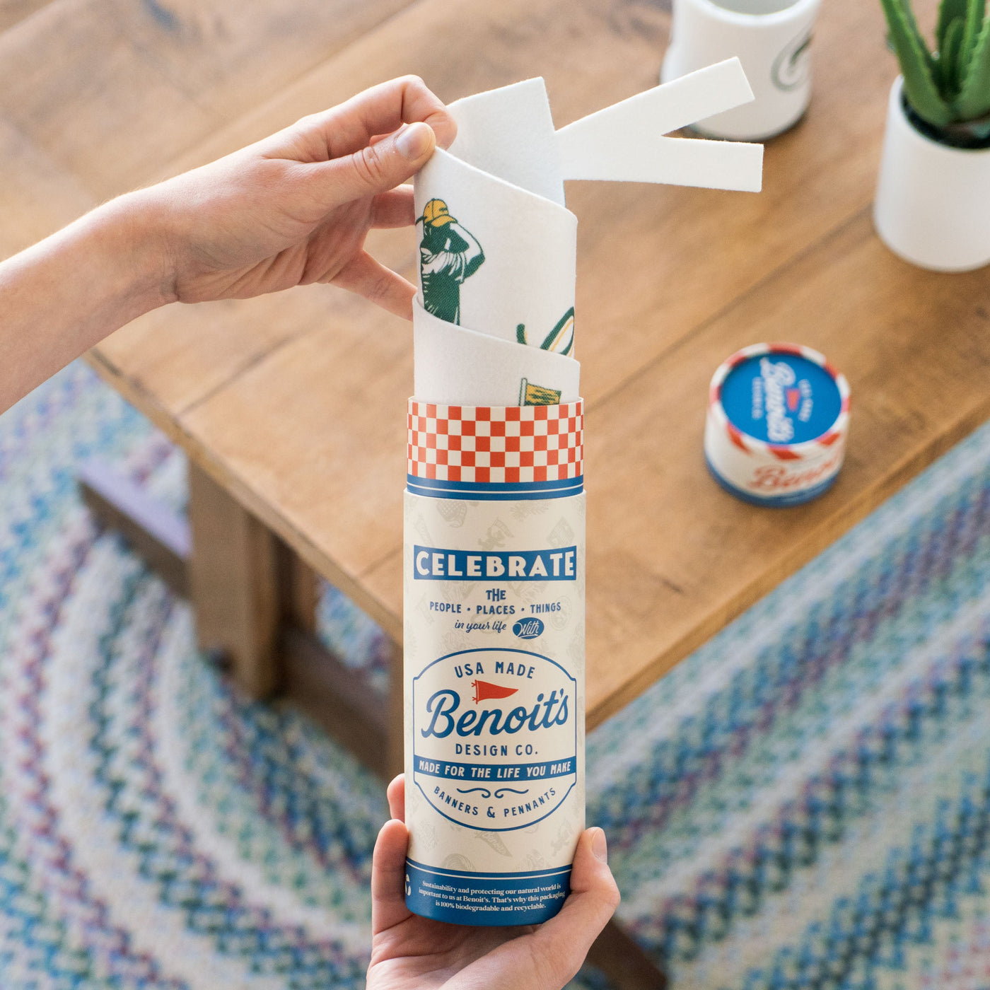 A person's hand is holding a tube of Benoît's design co. napkins, which are decorated with illustrations of people and various objects.