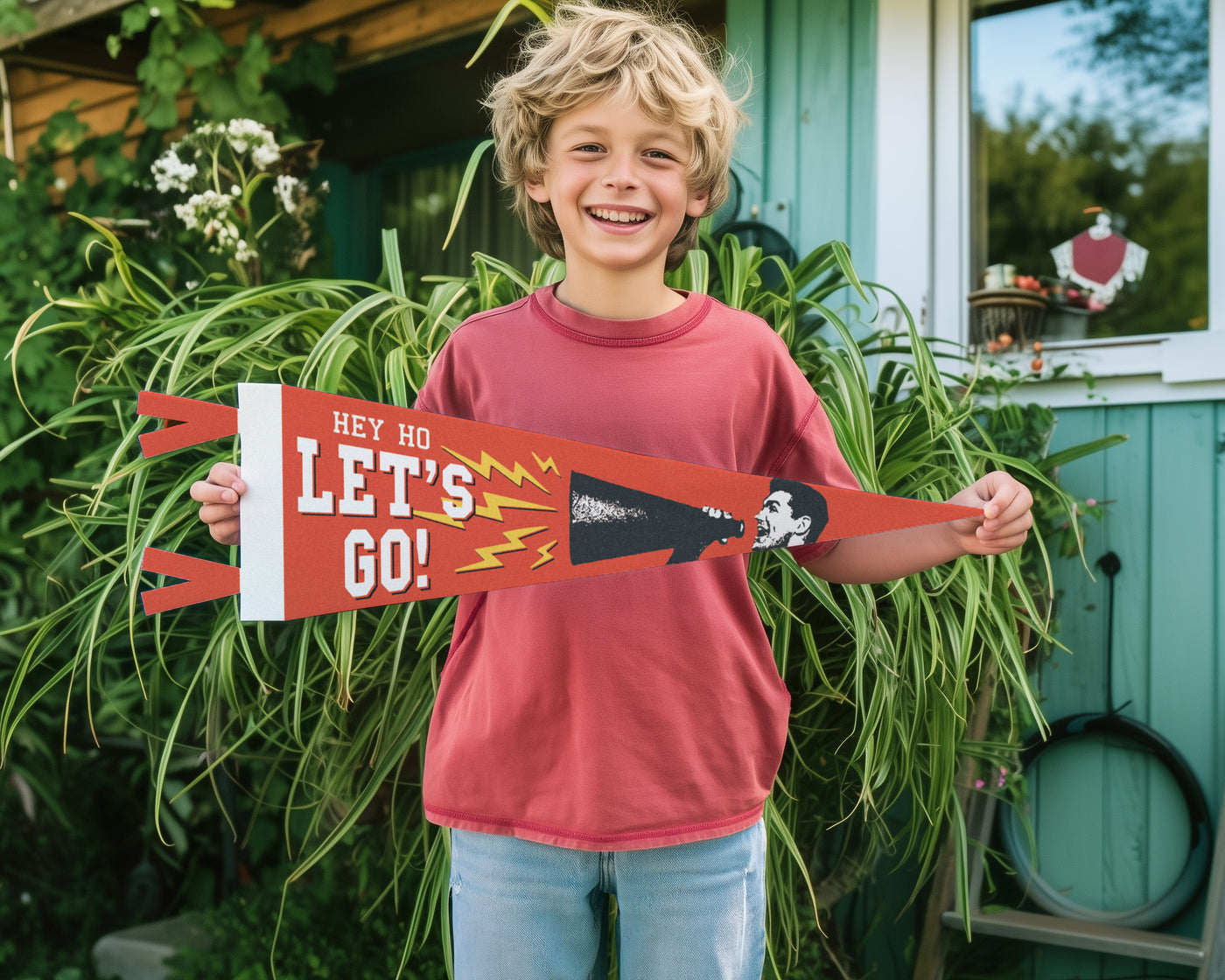 A young boy is holding up a red and white sign with the text "Hey ho let's go!" in front of a green building.