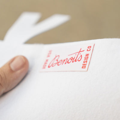A hand holding a white piece of paper with a red label that says "Benoits DESIGN CO".