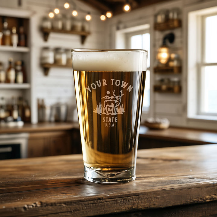 A glass of beer with the text "YOUR TOWN STATE USA" printed on it, sitting on a wooden surface in a bar setting.