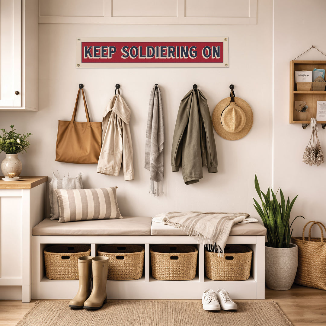 A cozy entryway with a bench, storage bins, and a sign that reads "KEEP SOLDIERS ON". The room has a warm and inviting atmosphere, with various accessories and decor elements such as a potted plant, a vase, and a hat.